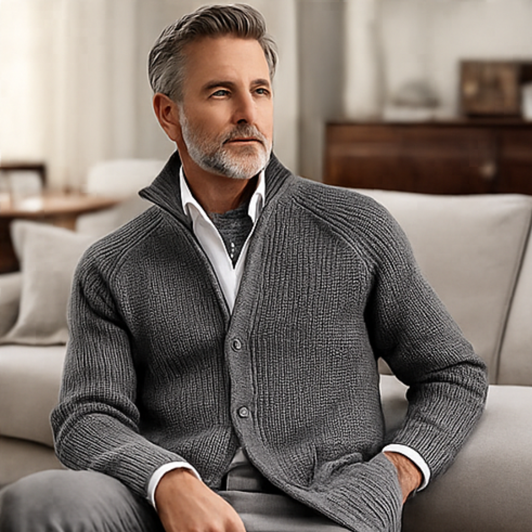 Man wearing a gray sweater sitting on a couch in a living room.