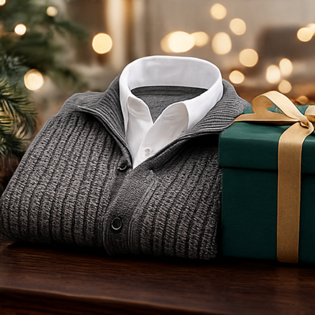 Folded gray sweater with white shirt collar next to a green gift box with a gold ribbon, against a blurred festive background.